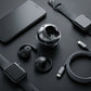 CTRL8 T2 over-the-ear earbuds with UNBLOQ technology and sleek charging case displayed alongside smartwatches and a smartphone on a matte black surface